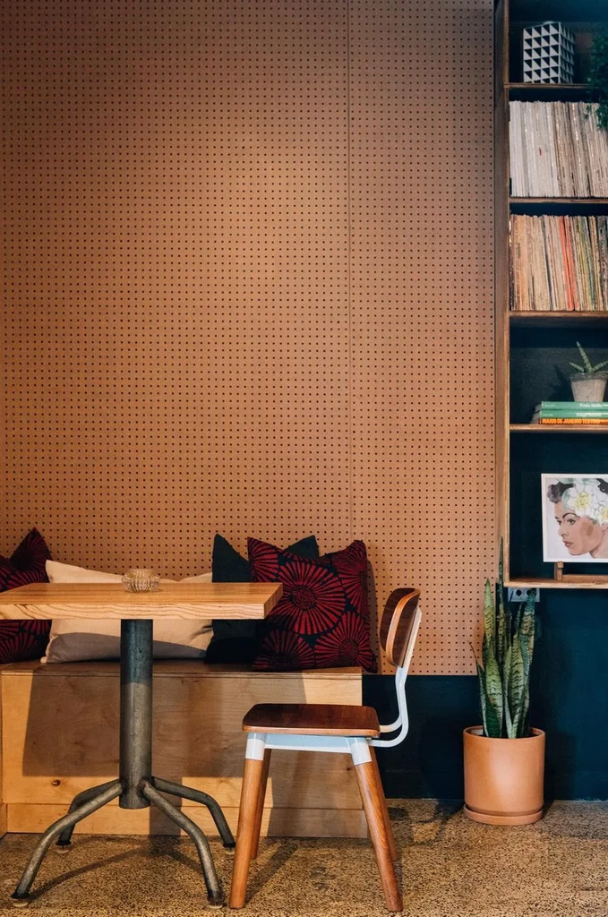 Cozy cafe corner with pegboard, bench, table, and bookshelf.