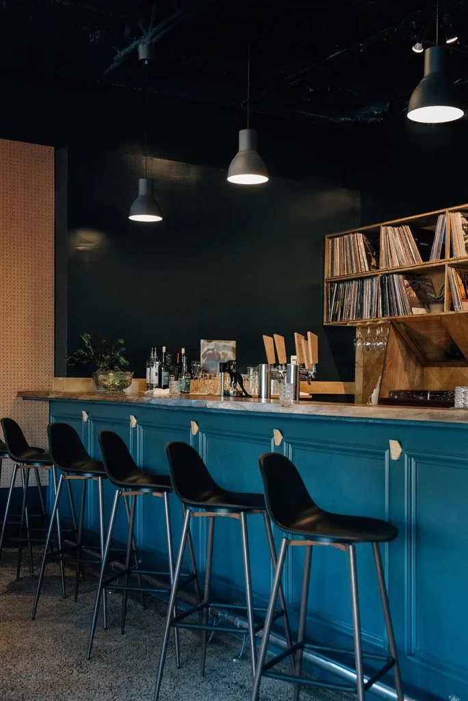 Stylish bar interior with teal counter, black stools, and vinyl records.