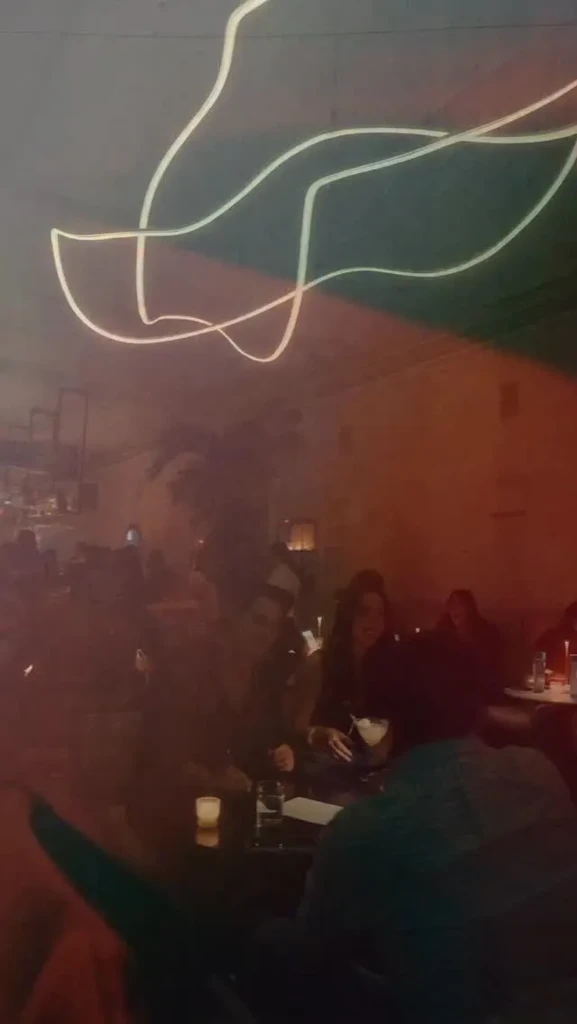 Dark restaurant with patrons, lit candle, and abstract ceiling lights.