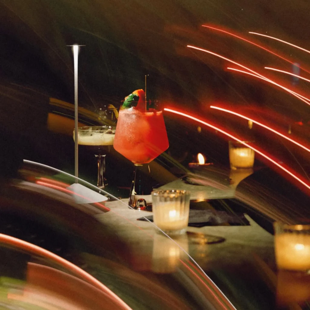 Red cocktail with another drink, candles, and red light streaks.