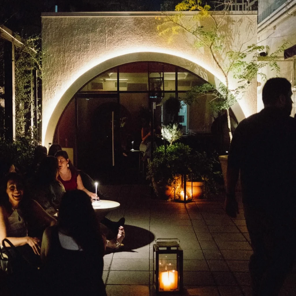 Restaurant patio at night with arched wall and people dining.