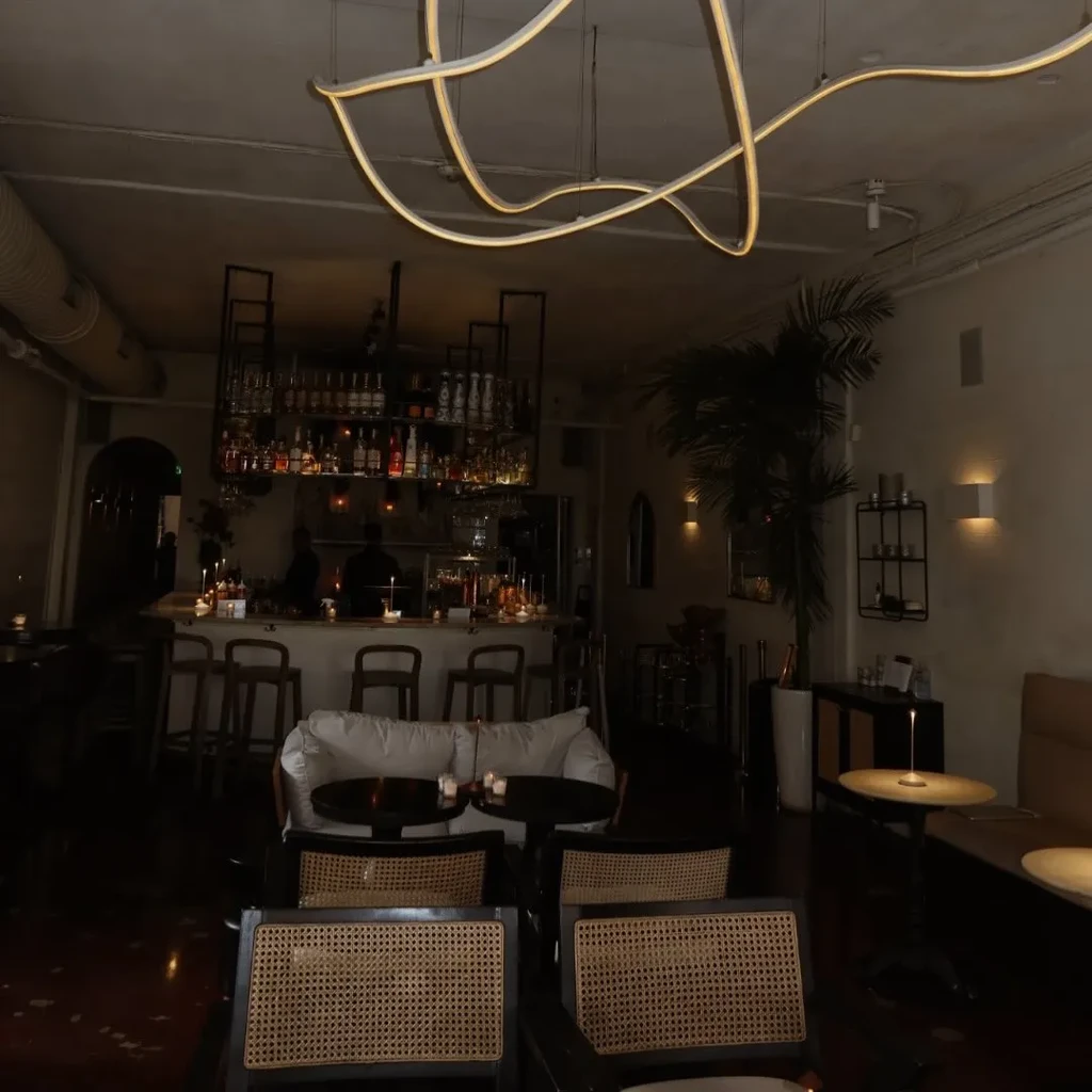Dimly lit bar with liquor shelves, bar stools, and seating.