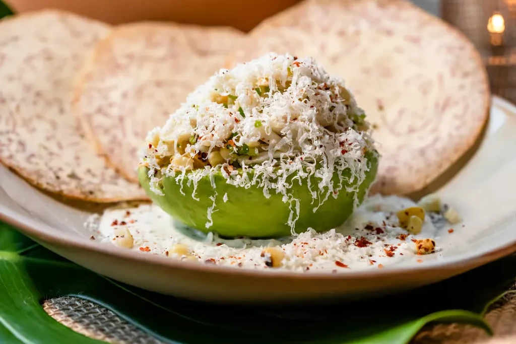 Avocado half topped with cheese, corn, and red spice on a plate.