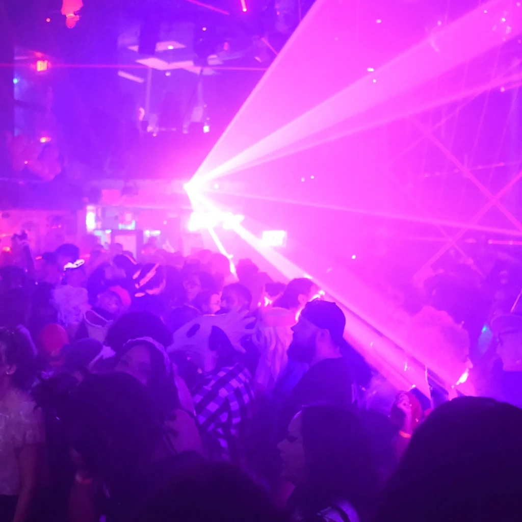 Crowded dance floor bathed in purple and pink laser lights.