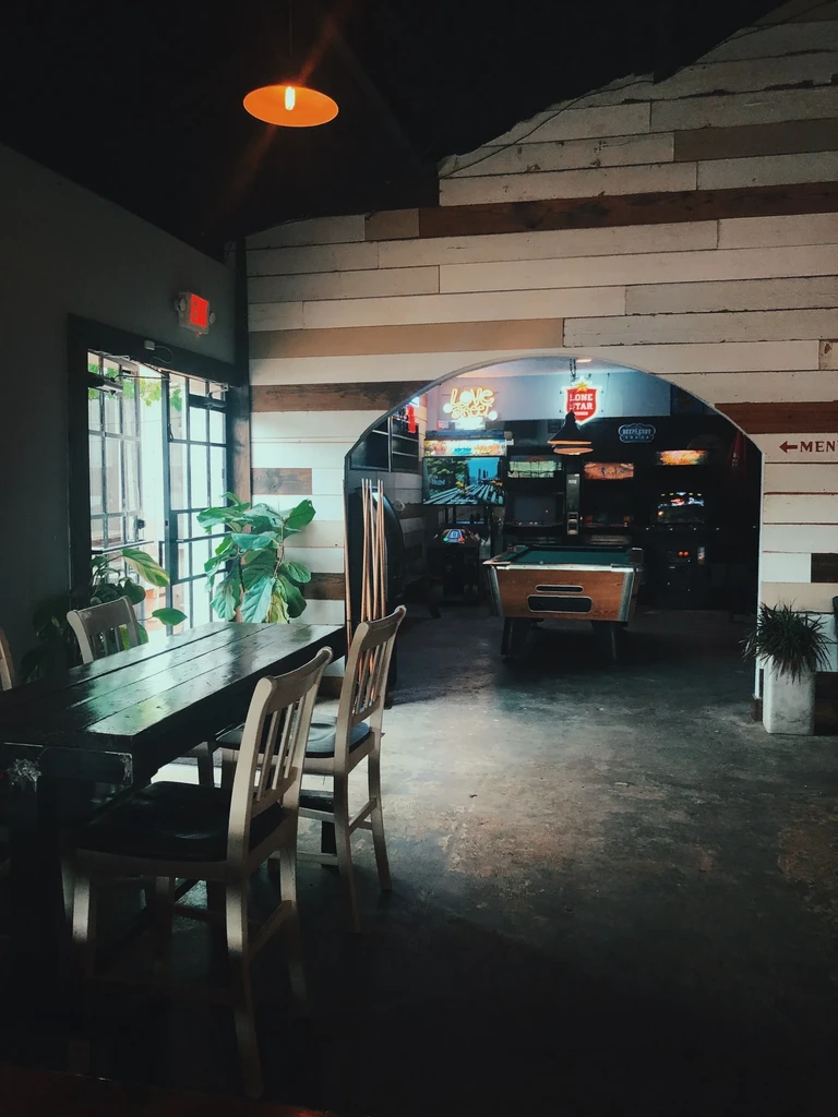 Rustic bar interior with tables, arcade games, and a pool table.