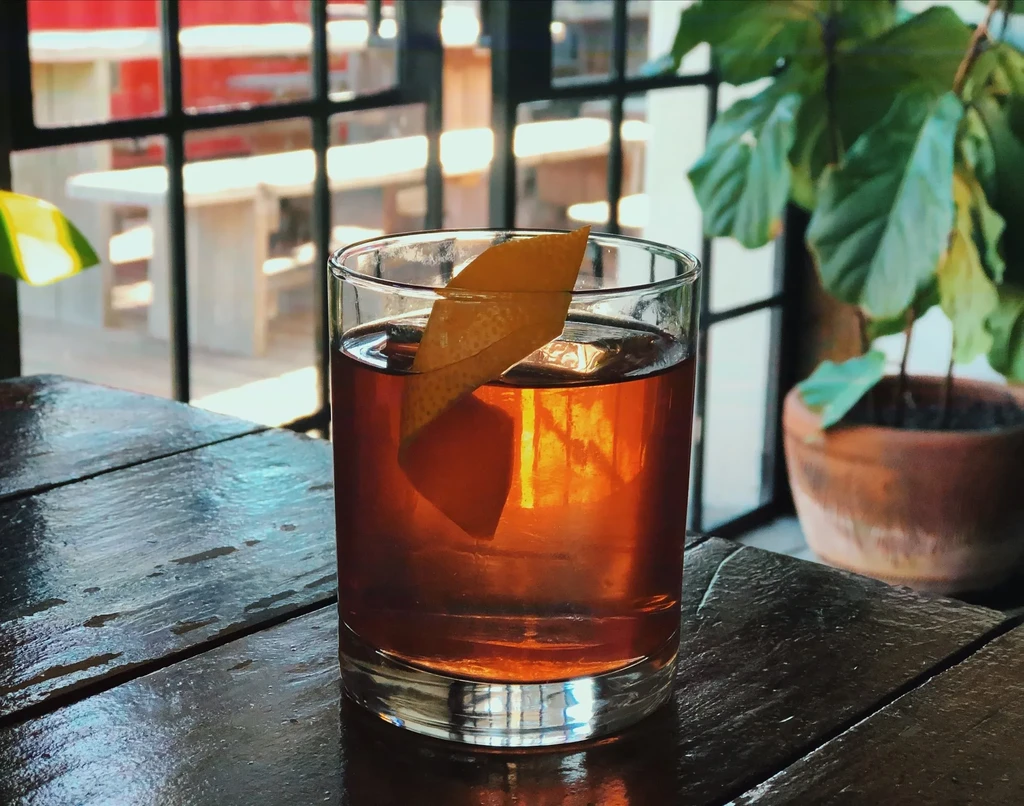 Amber cocktail in a clear glass with a citrus peel garnish.
