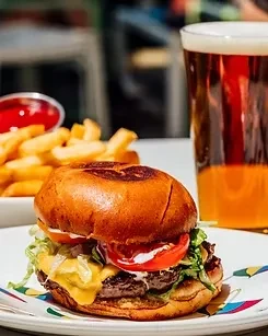 Gourmet burger, french fries, ketchup, and beer on a white plate.