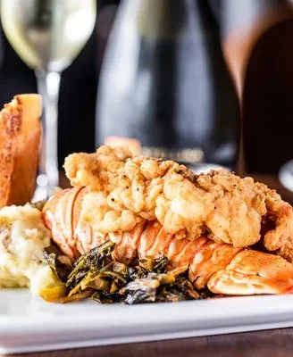 Gourmet lobster tail with fried seafood, mashed potatoes, and greens.