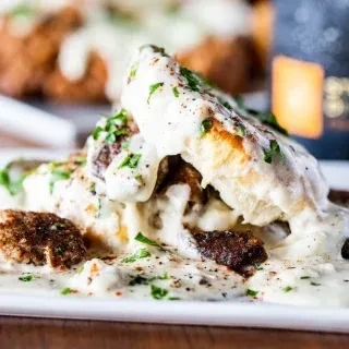 Biscuits and gravy with herbs and meat on a white plate.