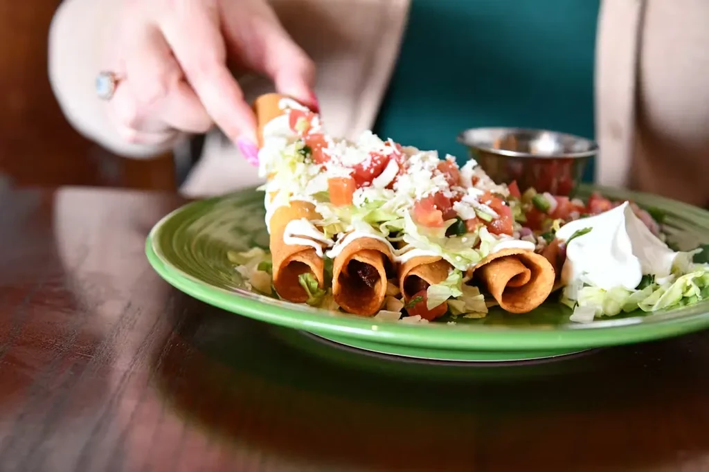 Close-up of a hand picking up a taquito from a green plate.