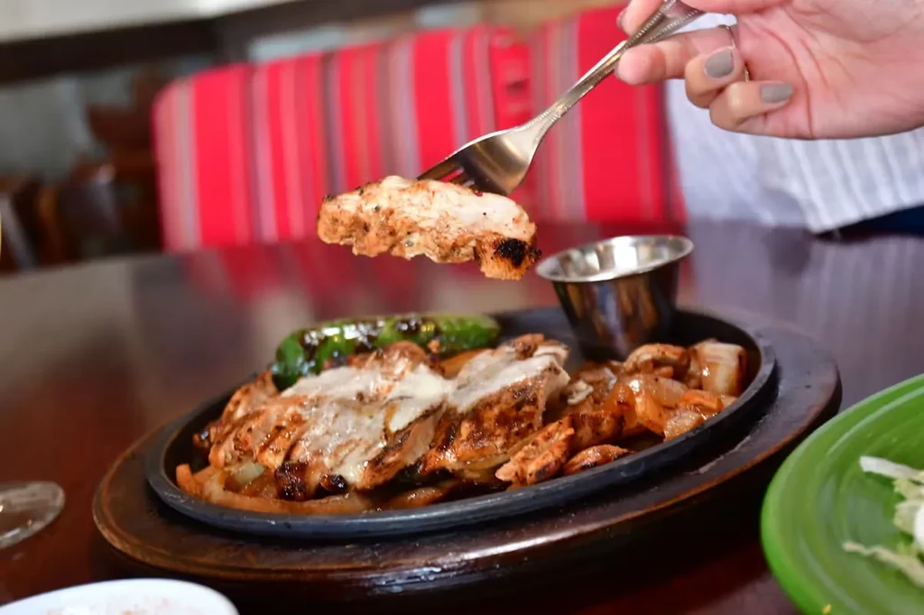 Sizzling chicken fajitas on a cast-iron skillet, with a fork lifting chicken.