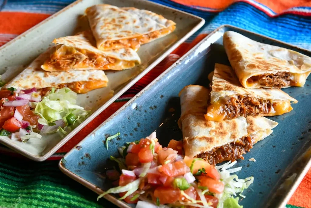 Two plates of quesadillas with pico de gallo and shredded lettuce.