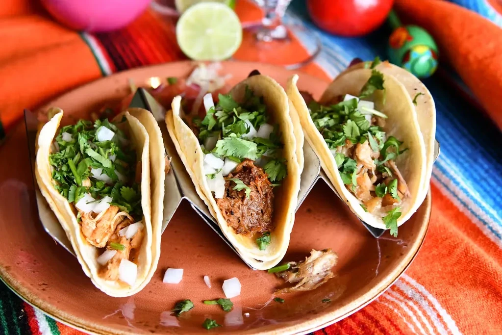 Three tacos on a plate, topped with cilantro and onions.