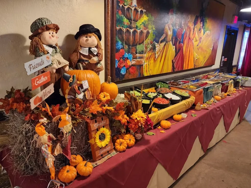Buffet table with autumn decorations, pilgrim scarecrows, and prepared food.
