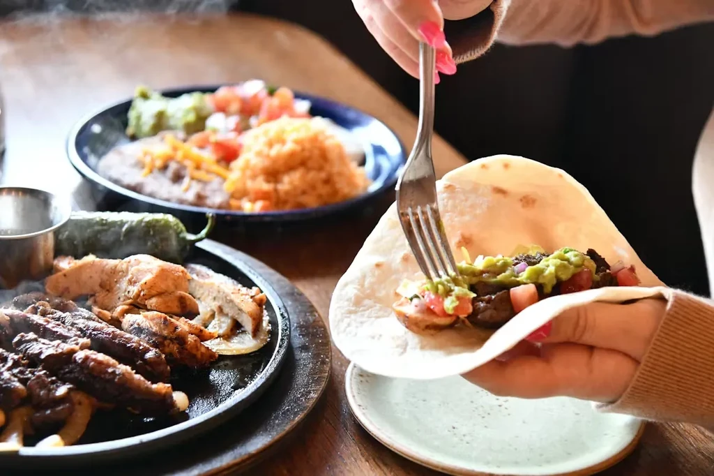 Person's hands assembling a taco or fajita with grilled meat.