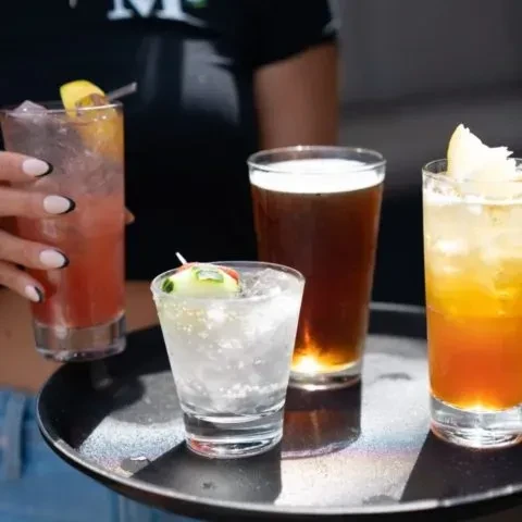 Close-up of a black tray holding four cocktails and a beer.
