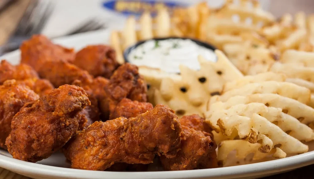 Plate of reddish-orange buffalo wings, waffle fries, and dipping sauce.