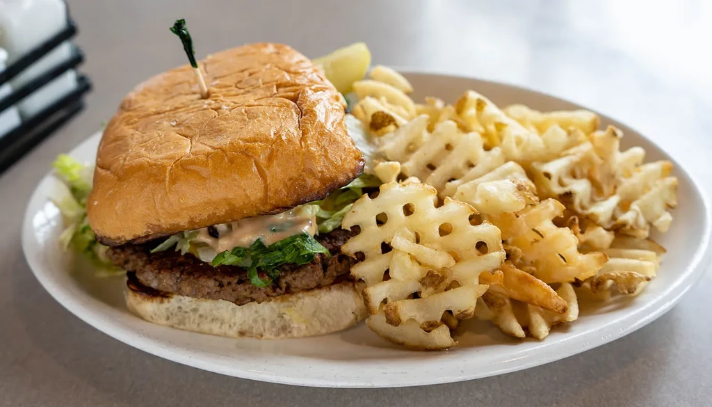 Burger with lettuce, sauce, waffle fries, and a lime wedge.