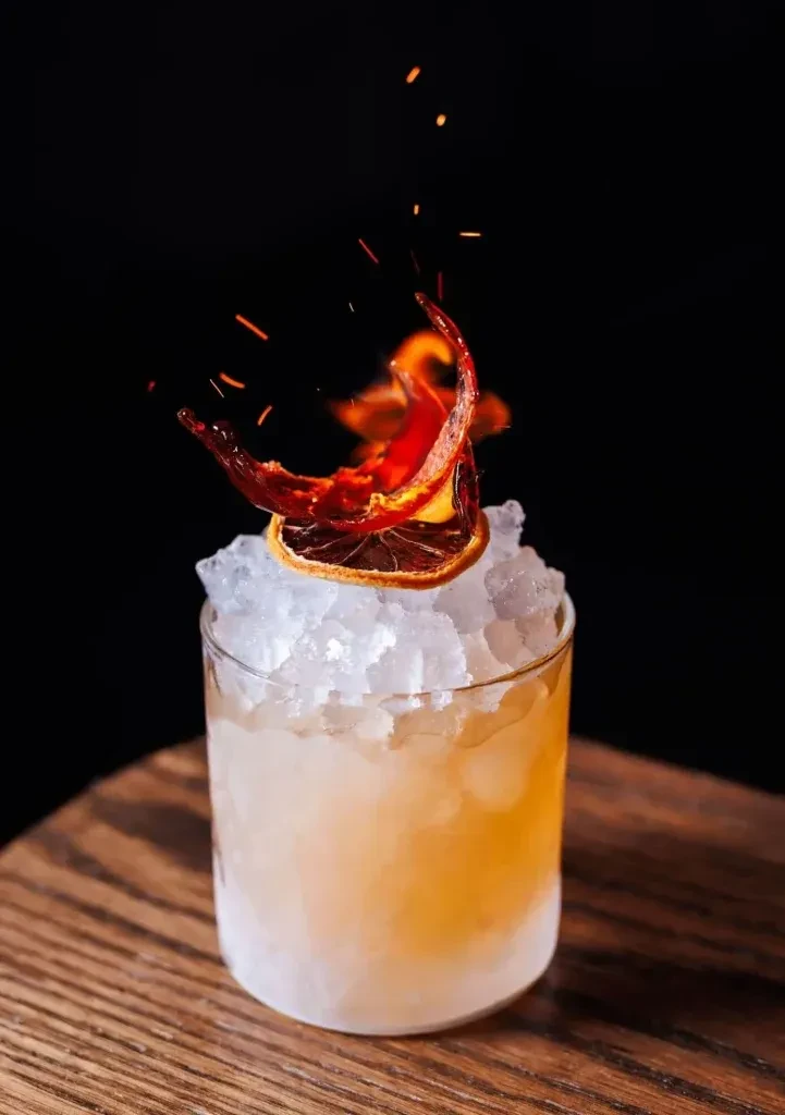 Cocktail in a frosted glass with an ignited orange garnish.