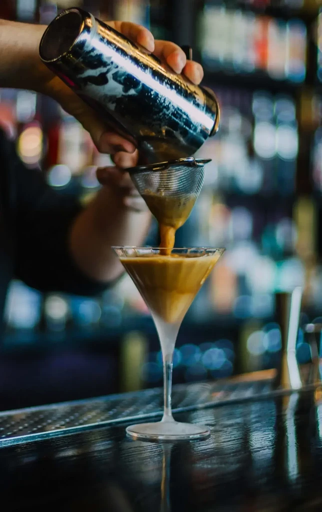 Bartender pours coffee-colored drink from shaker into martini glass.
