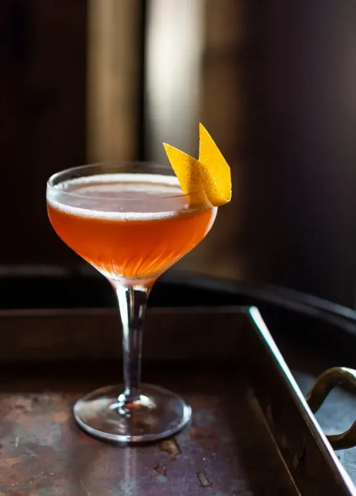 Orange-amber cocktail in a coupe glass with an orange peel garnish.
