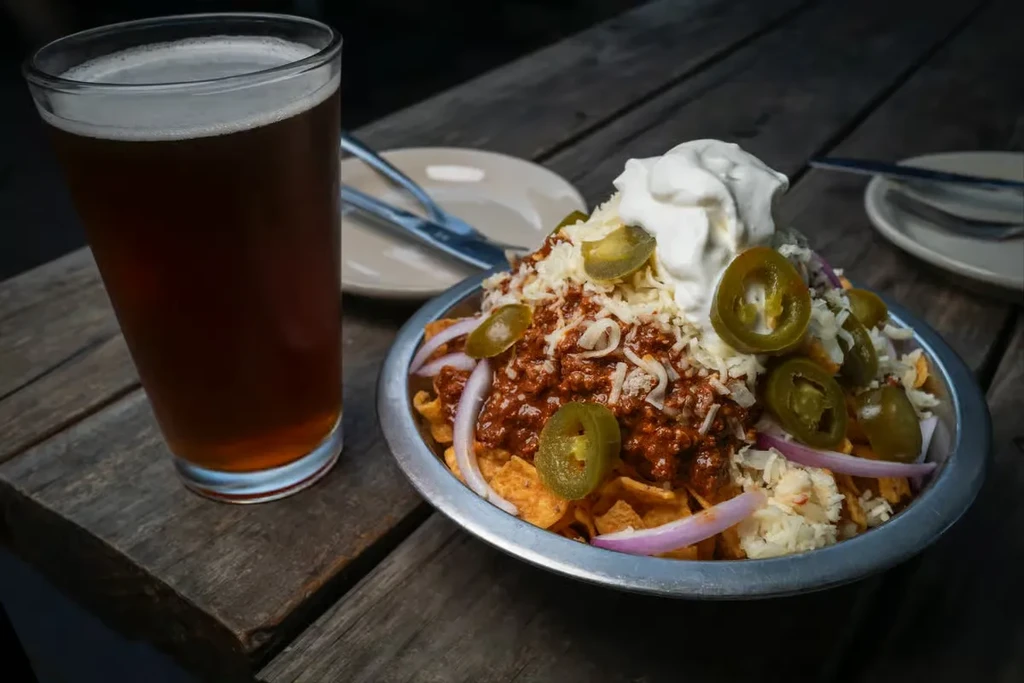 Nachos with toppings in a bowl, beer in a pint glass.