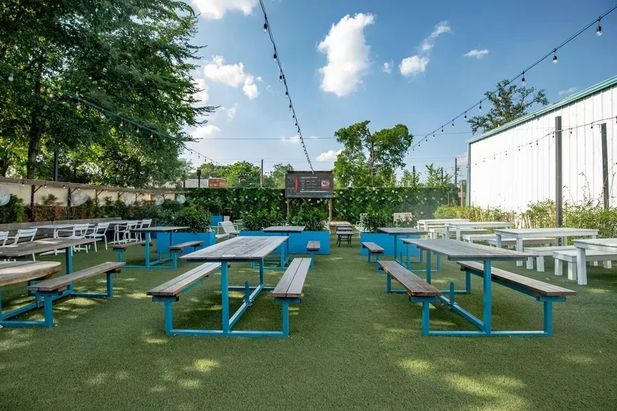 Outdoor dining area with picnic tables, artificial turf, and string lights.