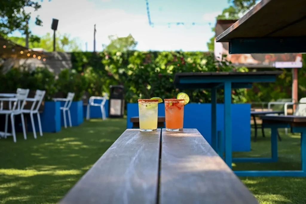 Two colorful cocktails on a wooden table at an outdoor restaurant.