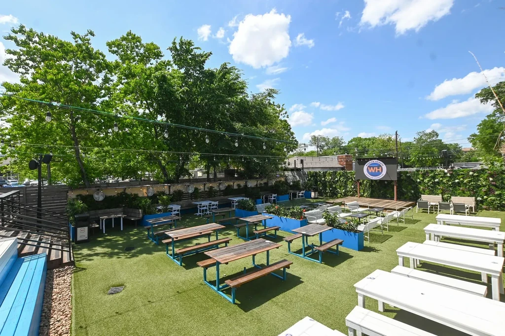 Outdoor dining area with picnic tables, stage, and string lights.