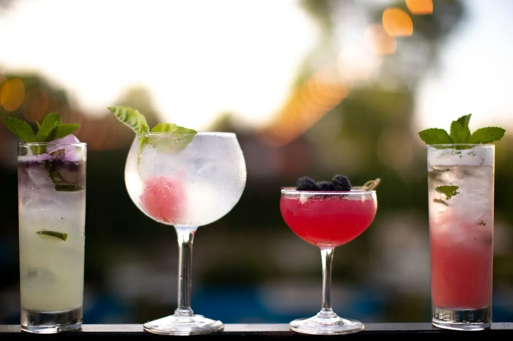 Four distinct cocktails in a row, with blurred outdoor background.