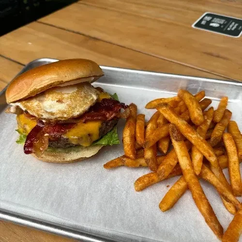 Gourmet burger with melted cheese, bacon, egg, and fries.
