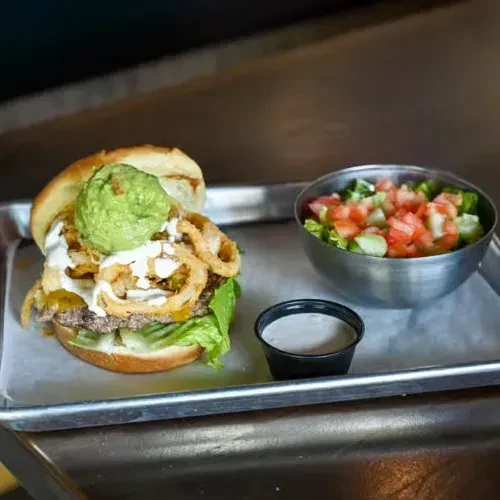 Burger with onion rings, guacamole, and a side salad.