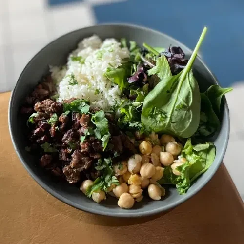 High-angle close-up of a food bowl with rice, meat, chickpeas, greens.