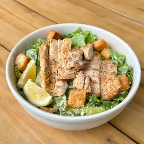 Caesar salad with grilled chicken, croutons, and lemon wedges.