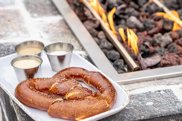 Salted pretzel and three dipping sauces on a patio.