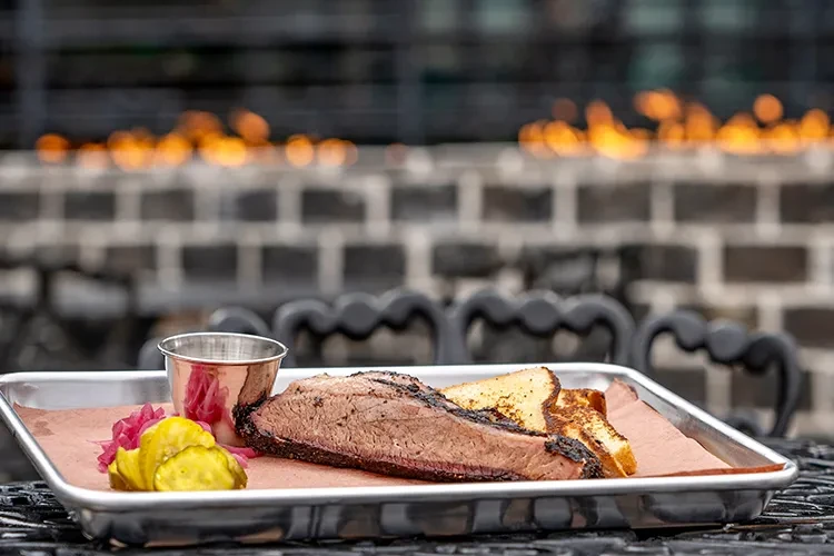 Smoked meat, toast, pickles, and sauce on a metal tray.