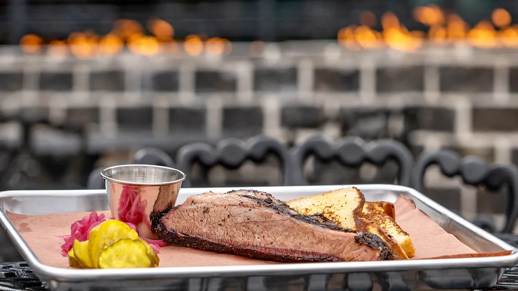 Smoked brisket, Texas toast, pickles, and pickled onions on a metal tray.