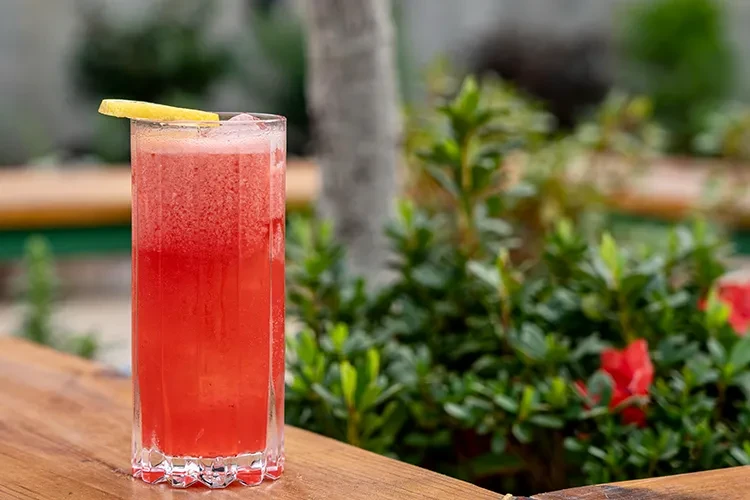 Red drink in a faceted glass with lemon, on a wooden surface.