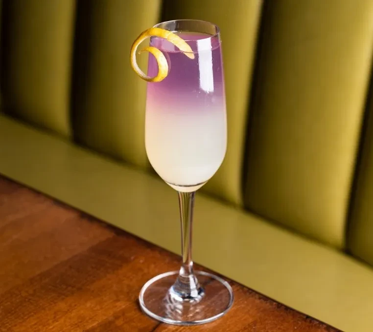 Champagne flute with layered purple and white cocktail, lemon peel.