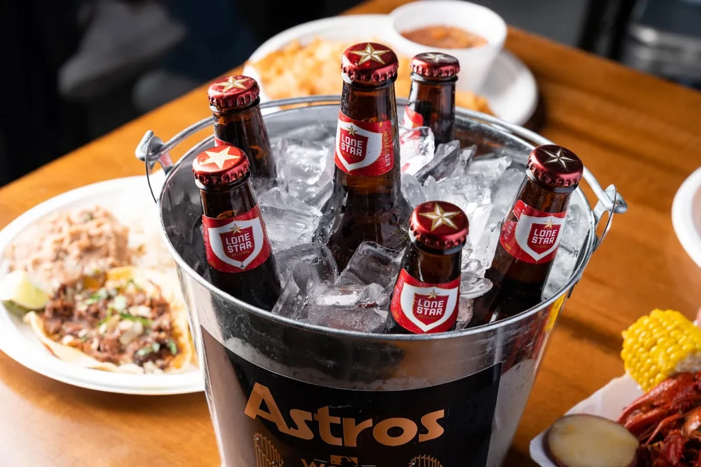 Bucket of Lone Star beer bottles and food on a wooden table.