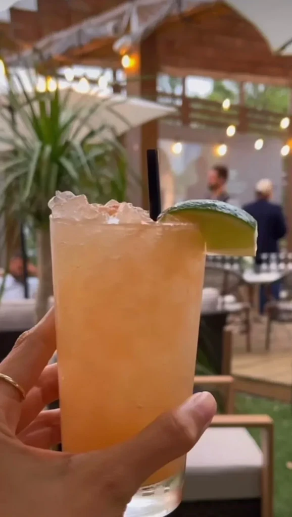Hand holds an orange drink with ice, lime, and straw.