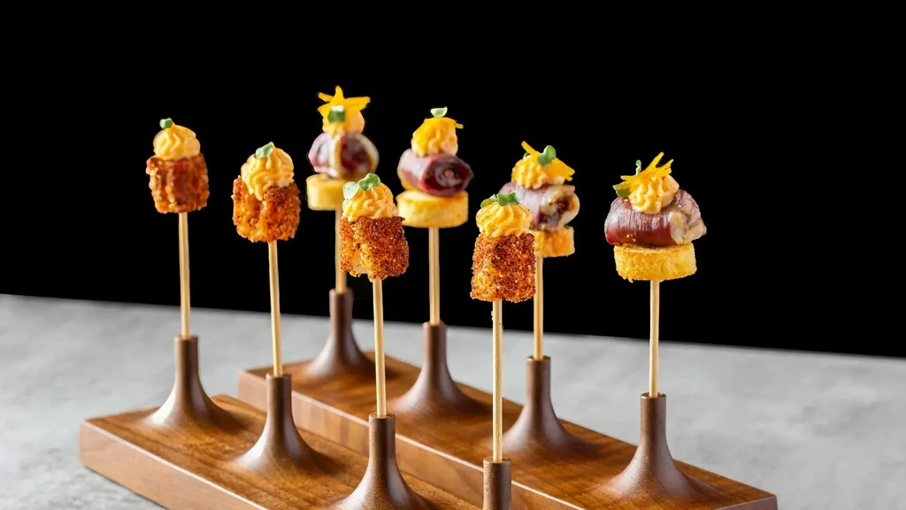 Eight gourmet appetizers on skewers with sauce, presented on a wooden tray.