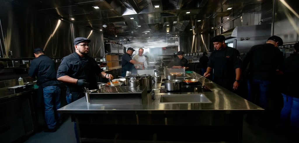 Professional kitchen with chefs cooking amidst stainless steel surfaces.