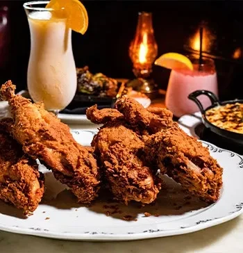 Crispy fried chicken on a white plate with drinks and a side dish.
