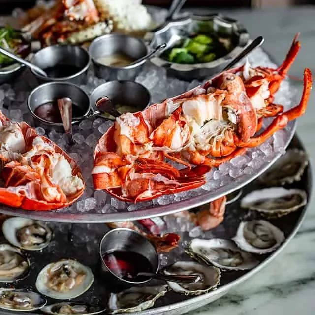 Multi-tiered seafood tower with lobster, oysters, clams, and sauces.