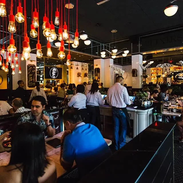 A restaurant or bar interior with patrons, staff, and warm lighting.