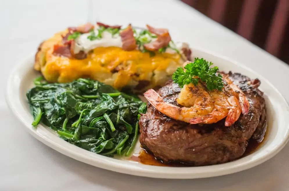 Surf and turf meal with baked potato and spinach on a white plate.