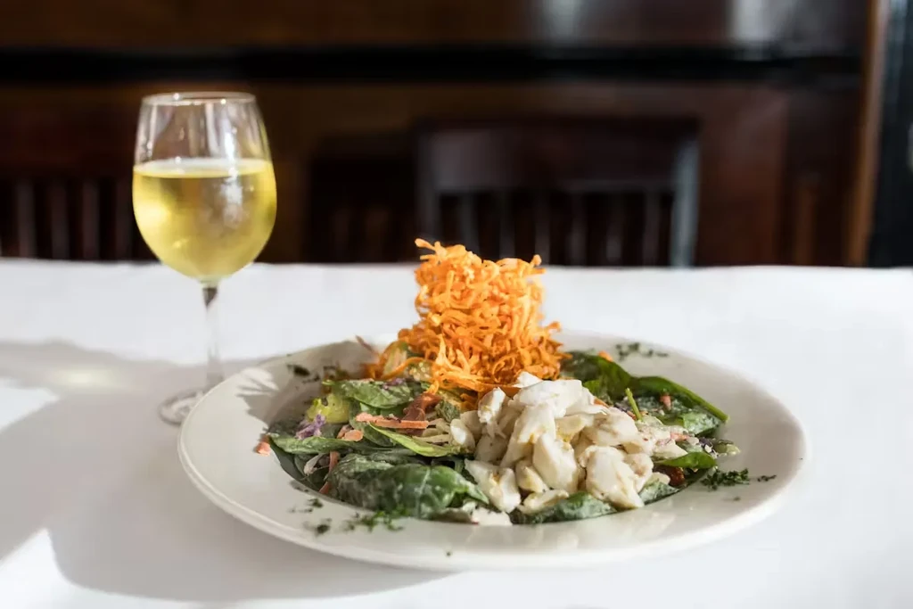 Salad with crab meat and crispy topping, and a glass of white wine.