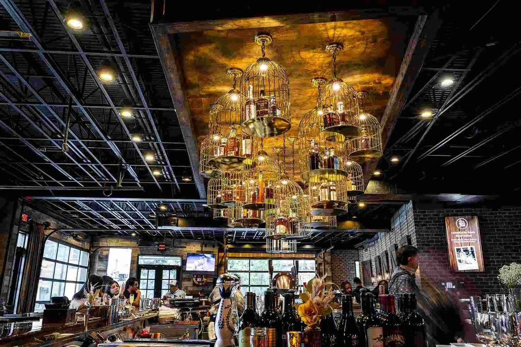 Birdcage chandeliers illuminate a dimly lit bar interior with patrons.