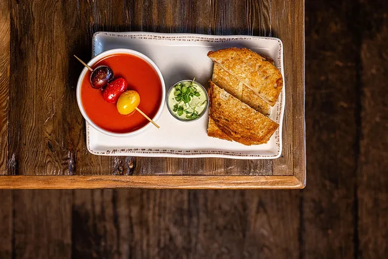 Tomato soup with bread and sauce on a wooden table.